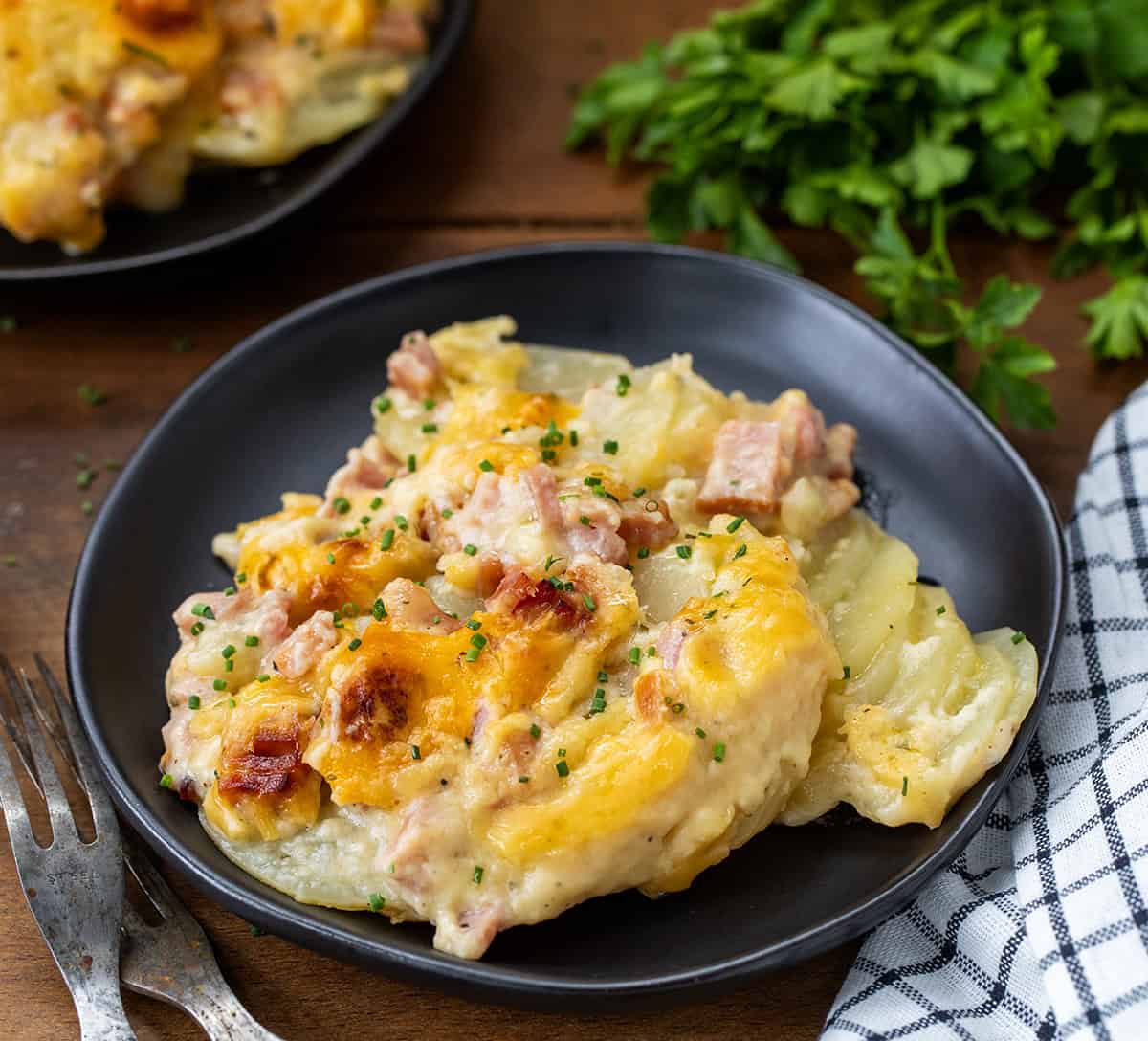 Black plates of Ranch Scalloped Potatoes and Ham on a wooden table close up.