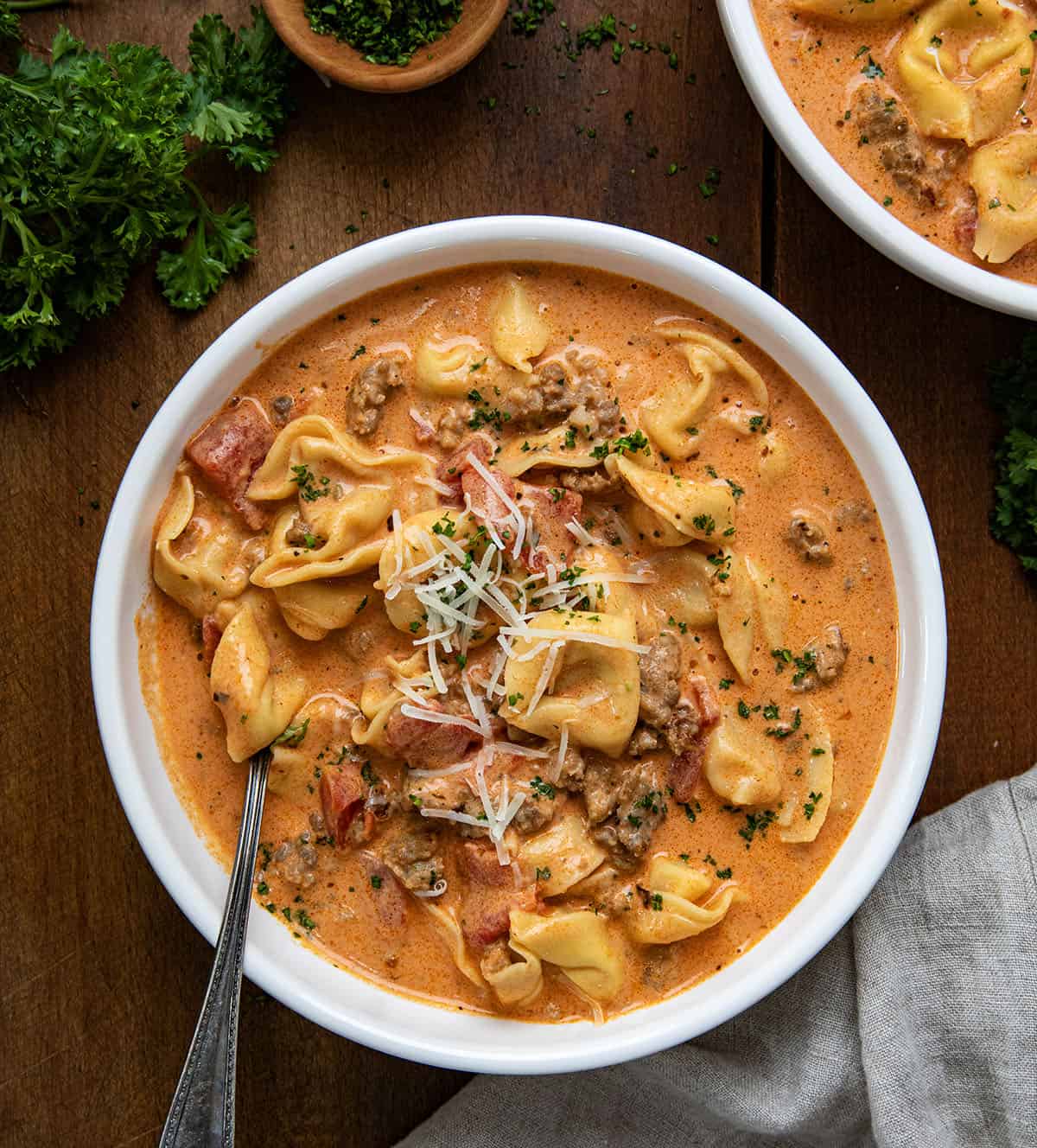 Bowls of Sausage Tortellini Soup on a wooden table from overhead.