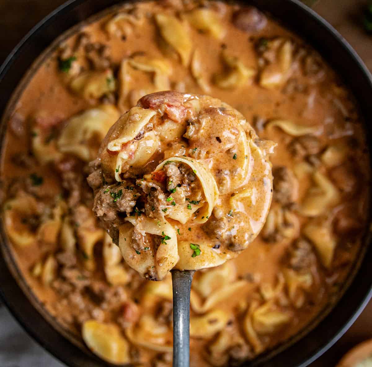 Ladle of Sausage Tortellini Soup being held above the pot and close up.