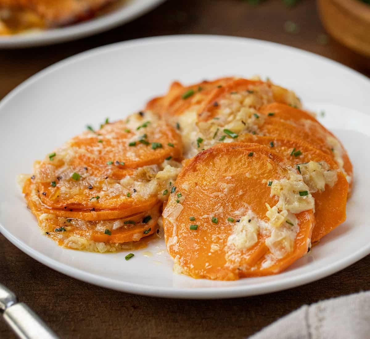 White plate of Scalloped Sweet Potatoes on a wooden table.