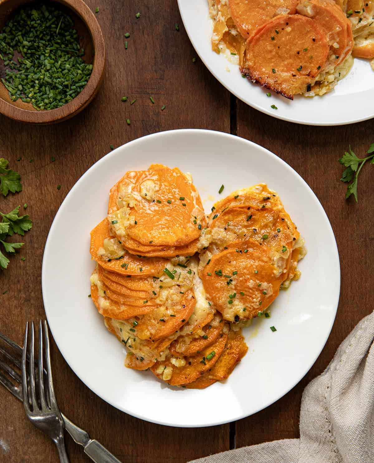 White plates of Scalloped Sweet Potatoes on a wooden table from overhead.