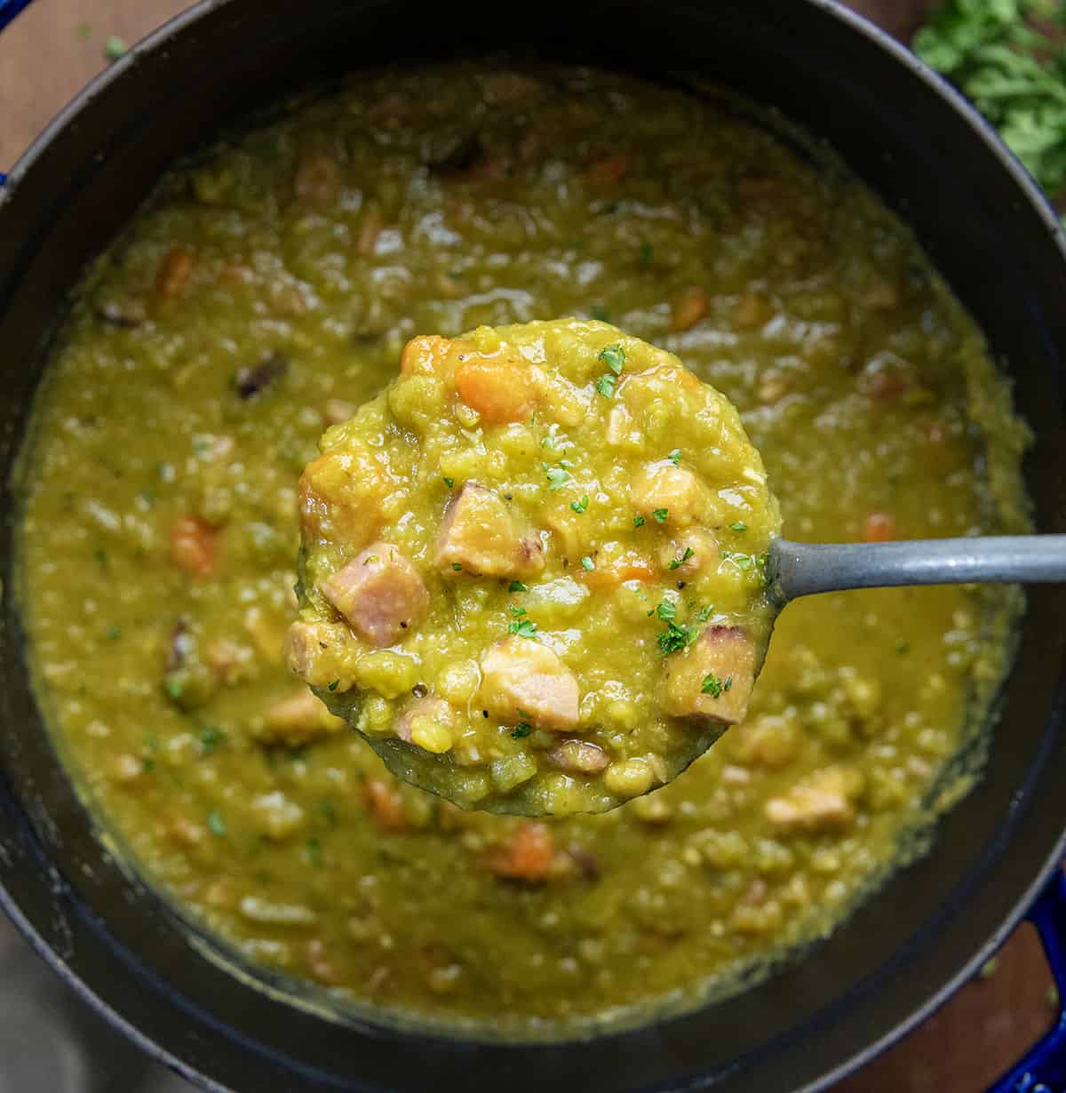 Holding a ladle full of Split Pea and Ham Soup over the pot.