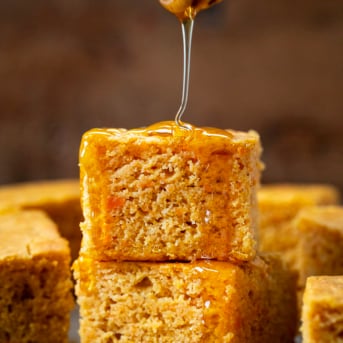 Drizzling honey over a stack of Sweet Potato Cornbread pieces.