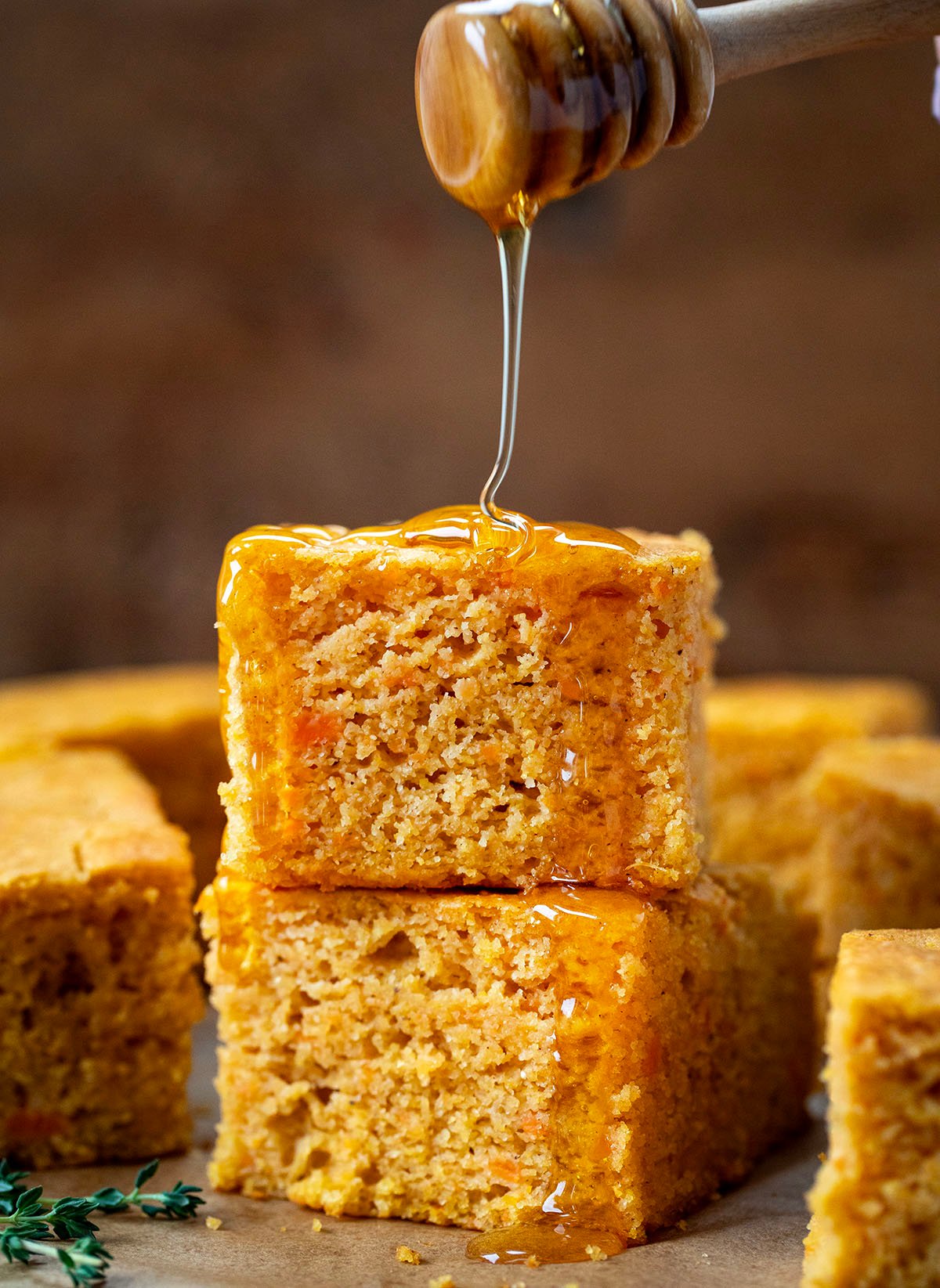 Drizzling honey over a stack of Sweet Potato Cornbread pieces.