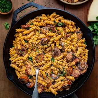 Skillet of Creamy Andouille Sausage Pasta with a spoon in it on a wooden table from overhead.