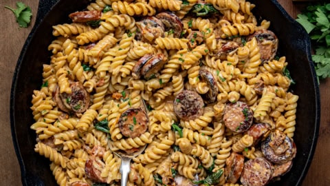Skillet of Creamy Andouille Sausage Pasta with a spoon in it on a wooden table from overhead.