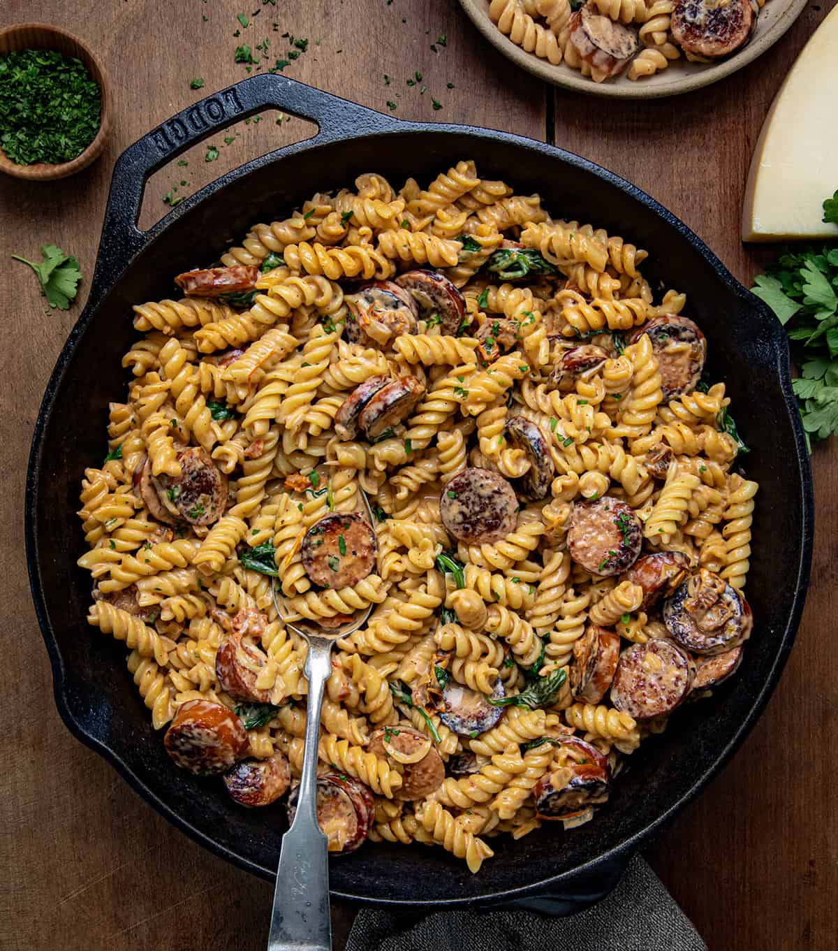 Skillet of Creamy Andouille Sausage Pasta with a spoon in it on a wooden table from overhead.