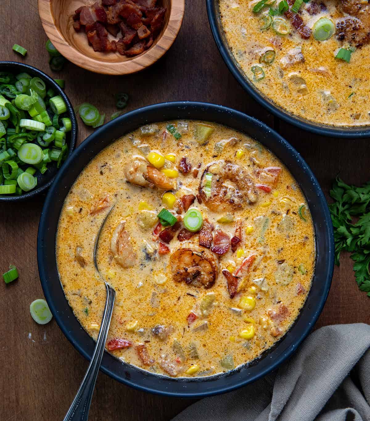 Bowls of Blackened Shrimp and Corn Chowder on a wooden table from overhead with one bowl with a spoon.