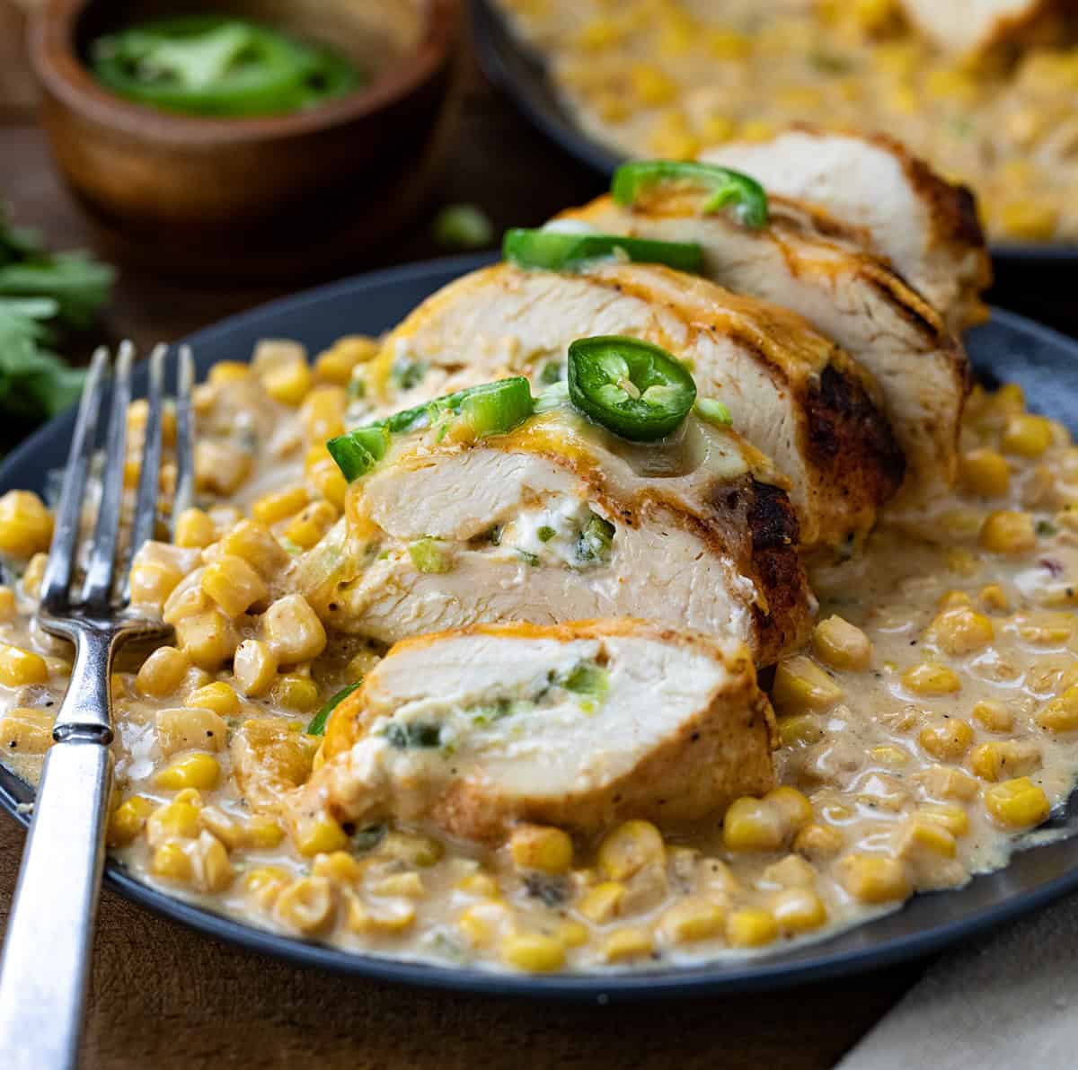 Sliced stuffed chicken breast of a bed of creamed corn on a plate.