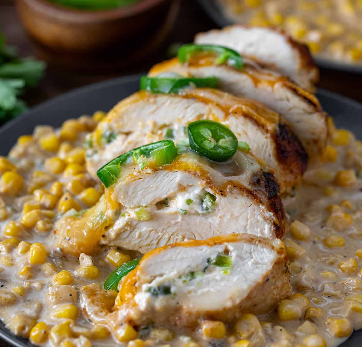 Sliced stuffed chicken breast of a bed of creamed corn on a plate.