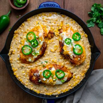 Skillet of Cheesy Jalapeno Stuffed Chicken and Creamed Corn on a wooden table from overhead.