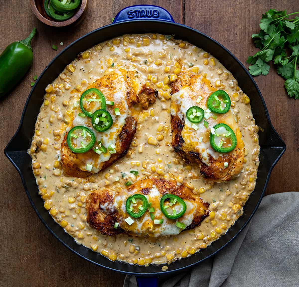 Skillet of Cheesy Jalapeno Stuffed Chicken and Creamed Corn on a wooden table from overhead.