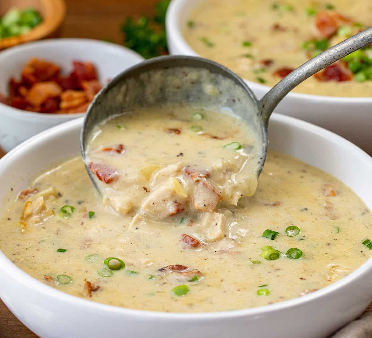 Pouring Chicken Bacon Potato Soup into a white bowl.