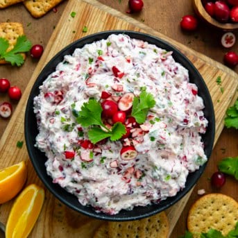 Black bowl of Creamy Cranberry Jalapeño Dip on a cutting board from overhead.