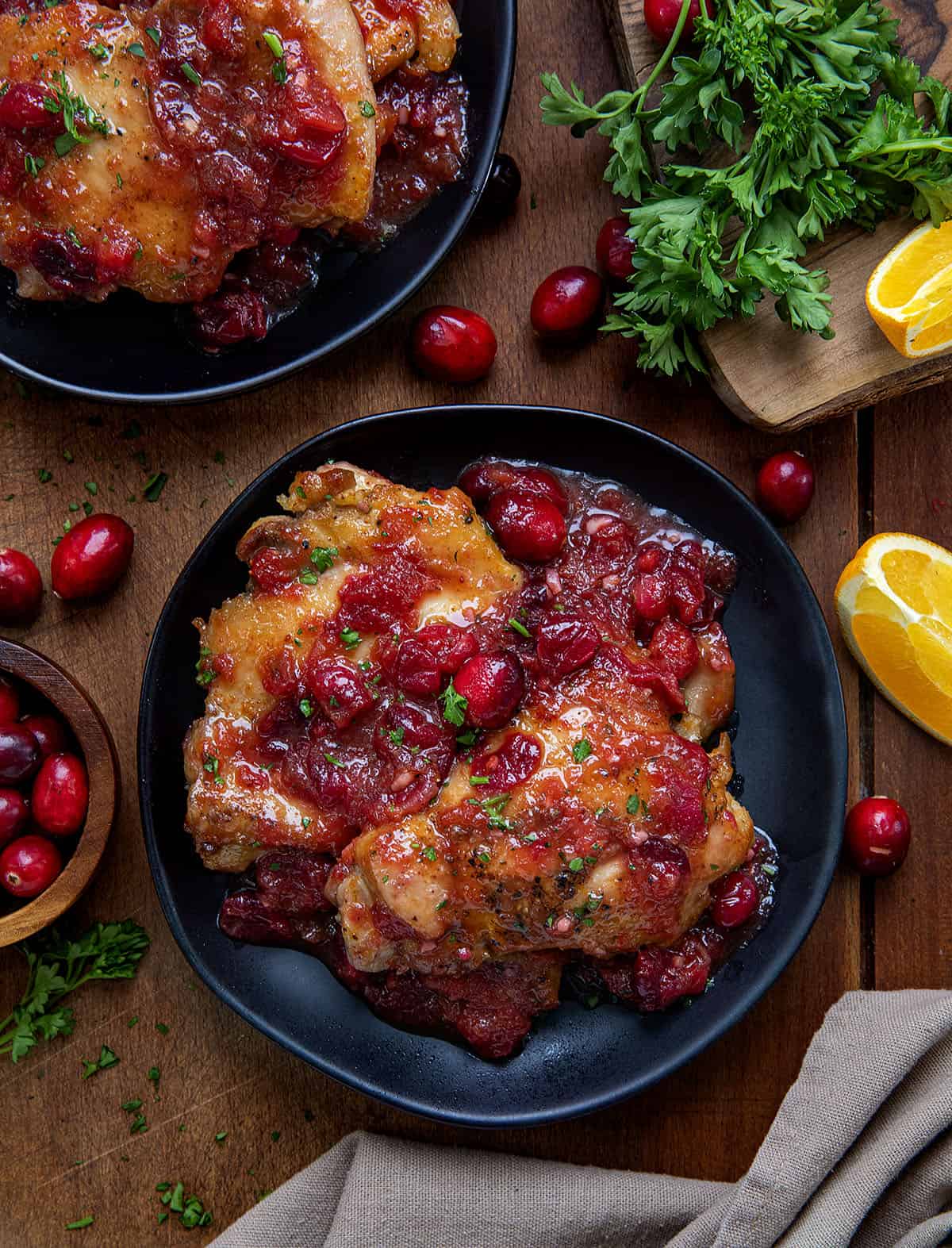 Black plates of Cranberry Orange Chicken in sauce on a wooden table from overhead.