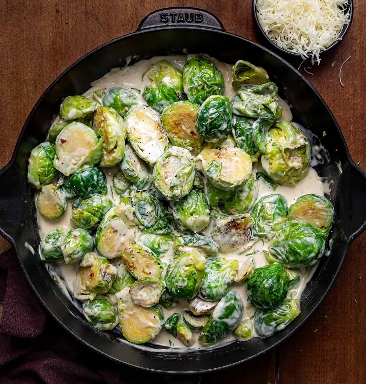 Skillet of Creamy Garlic Parmesan Brussels Sprouts on a wooden table. 