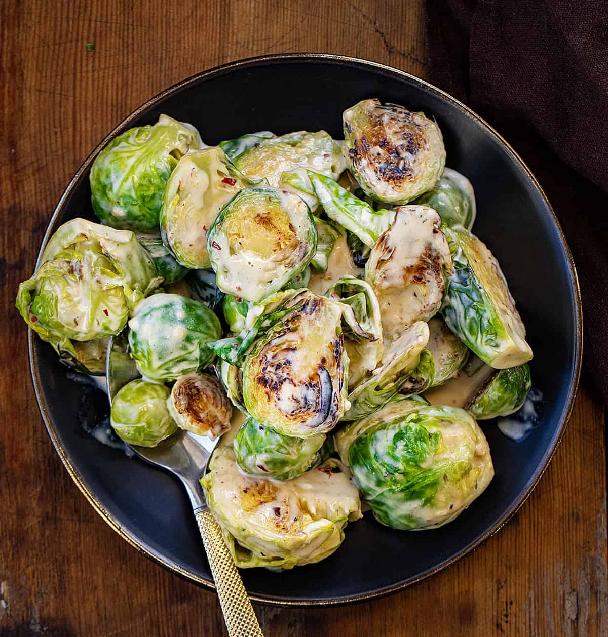 Creamy Garlic Parmesan Brussels Sprouts on a black plate with a gold spoon.