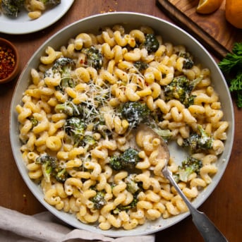 Skillet of Creamy Ricotta Pasta with Roasted Broccoli with a spoon in it on a wooden table from overhead.