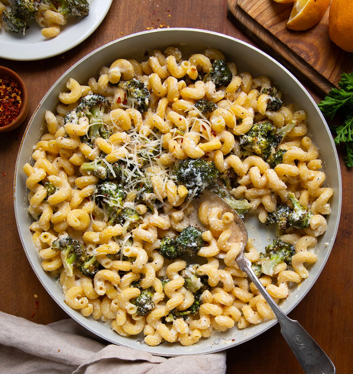 Skillet of Creamy Ricotta Pasta with Roasted Broccoli with a spoon in it on a wooden table from overhead.