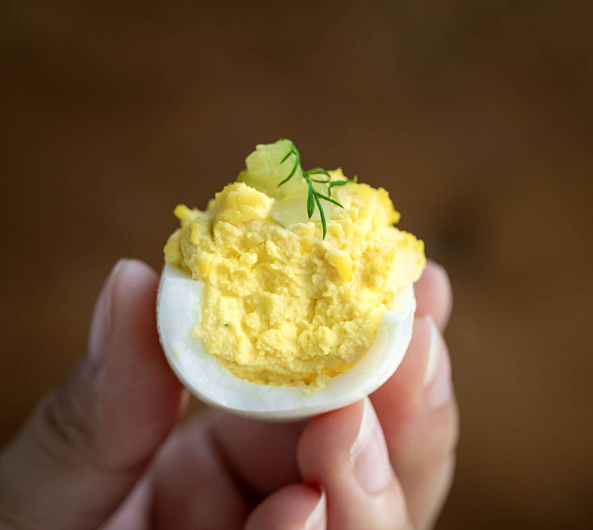 Hand holding a bit into Dill Pickle Deviled Egg.