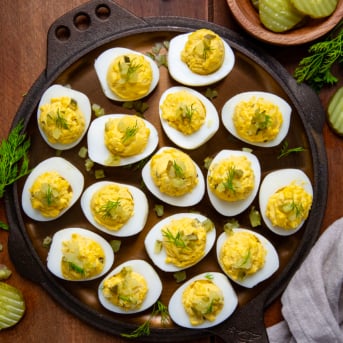 Dill Pickle Deviled Eggs on a wooden table from overhead with dill pickles and fresh dill around.