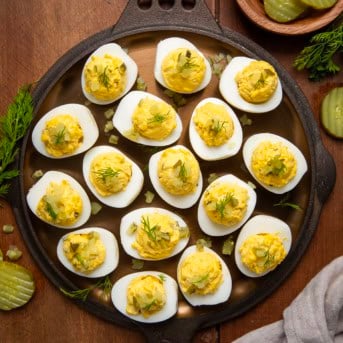 Dill Pickle Deviled Eggs on a wooden table from overhead with dill pickles and fresh dill around.