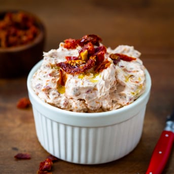 Close up of a bowl of Sun-Dried Tomato Dip on a wooden table.