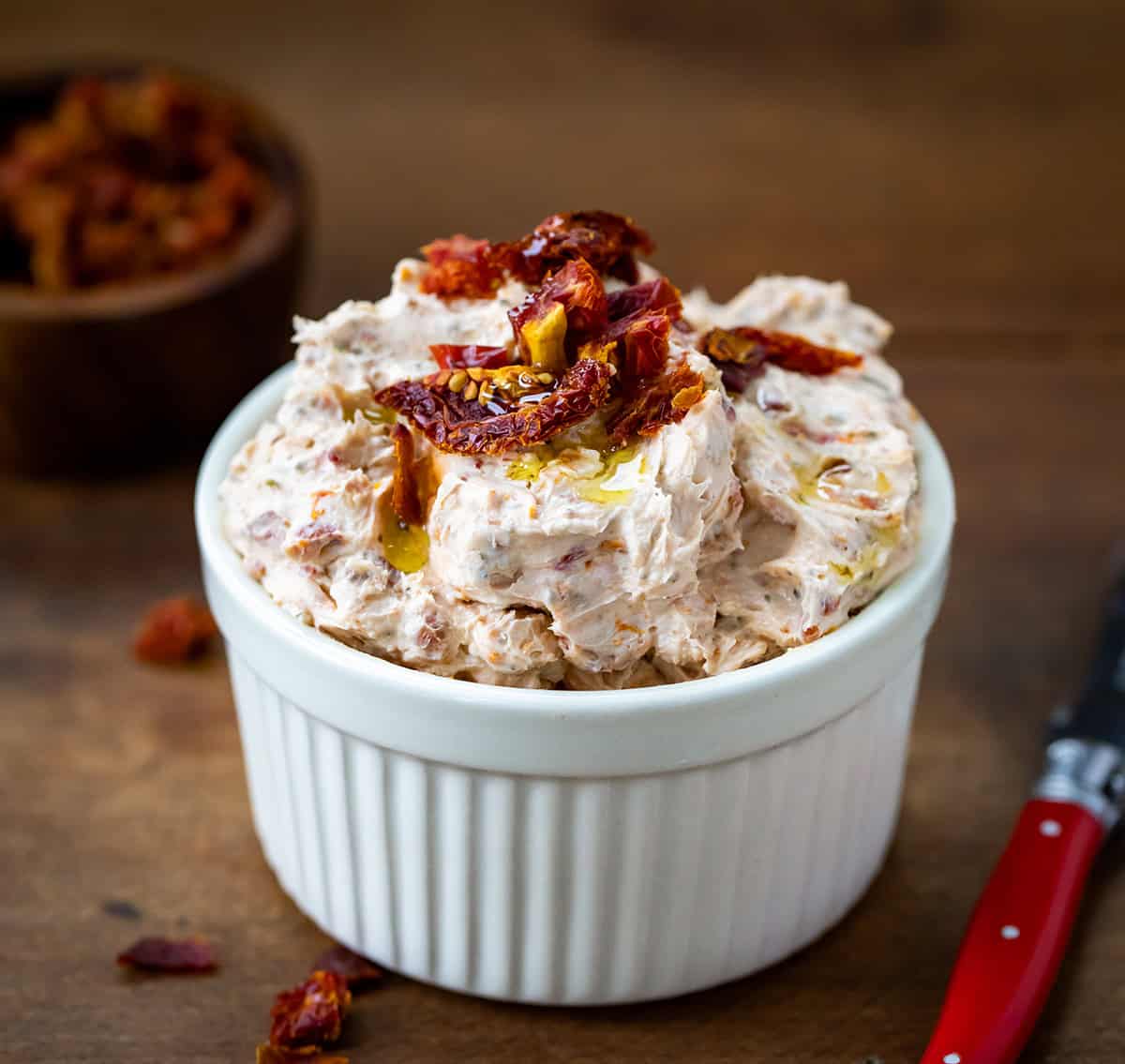 Close up of a bowl of Sun-Dried Tomato Dip on a wooden table. 