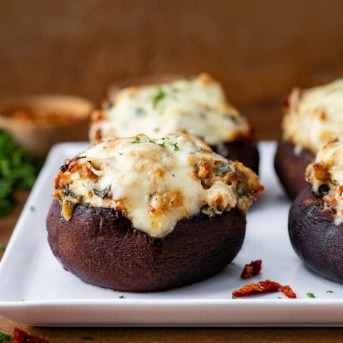 Tuscan Stuffed Mushroom Caps on a white platter on a wooden table.