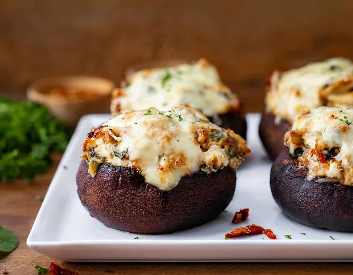 Tuscan Stuffed Mushroom Caps on a white platter on a wooden table. 