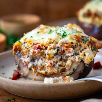 Cut in half Tuscan Stuffed Mushroom Cap on a plate with a fork resting on the plate.