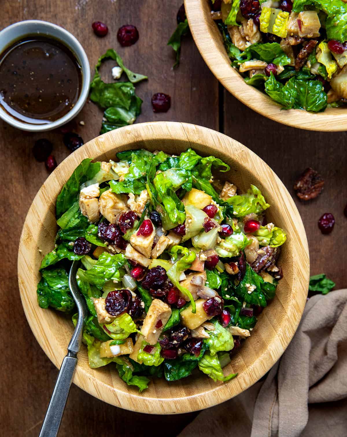 Bowls of Winter Chopped Salad with lettuce, apples, pomegranate, chicken, and feta on a wooden table.