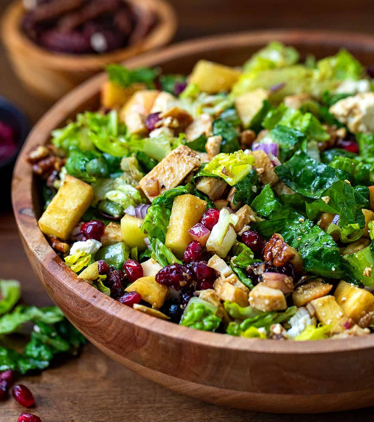 CLose up of Winter Chopped Salad with lettuce, apples, pomegranate, chicken, and feta on a wooden table.