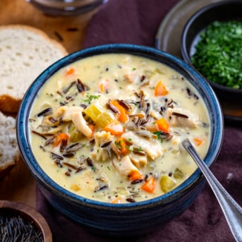 Blue bowl full of Chicken Wild Rice Soup with a spoon on a wooden table.