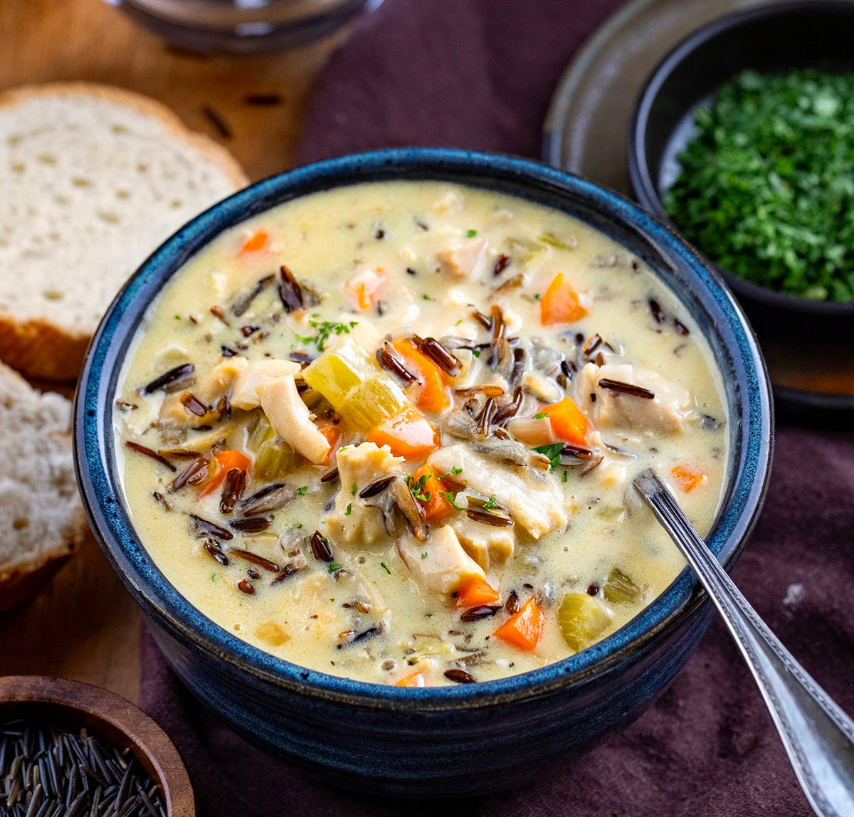 Blue bowl full of Chicken Wild Rice Soup with a spoon on a wooden table. 