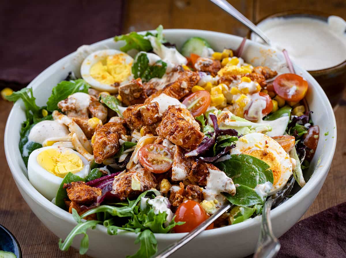 Bowl of Chipotle Chicken Cobb Salad on a wooden table focusing on the chicken pieces.