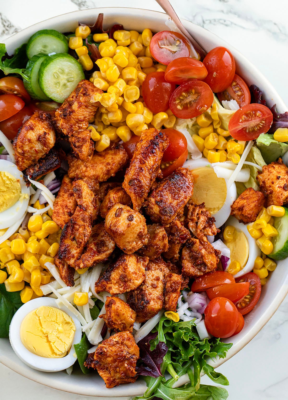 Bowl of Chipotle Chicken Cobb Salad with a spoon in it on a white marble counter.