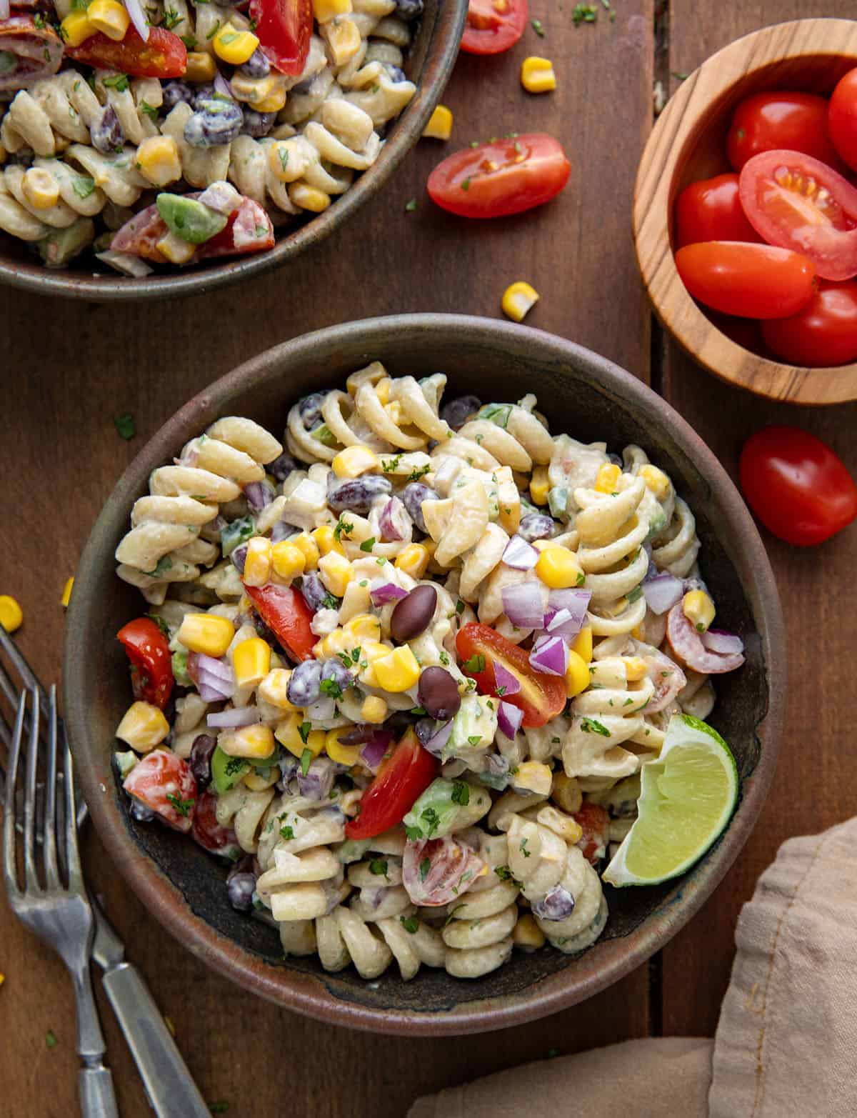 Bowls of Chipotle Lime Pasta Salad on a wooden table with lime and fresh cut tomatoes.