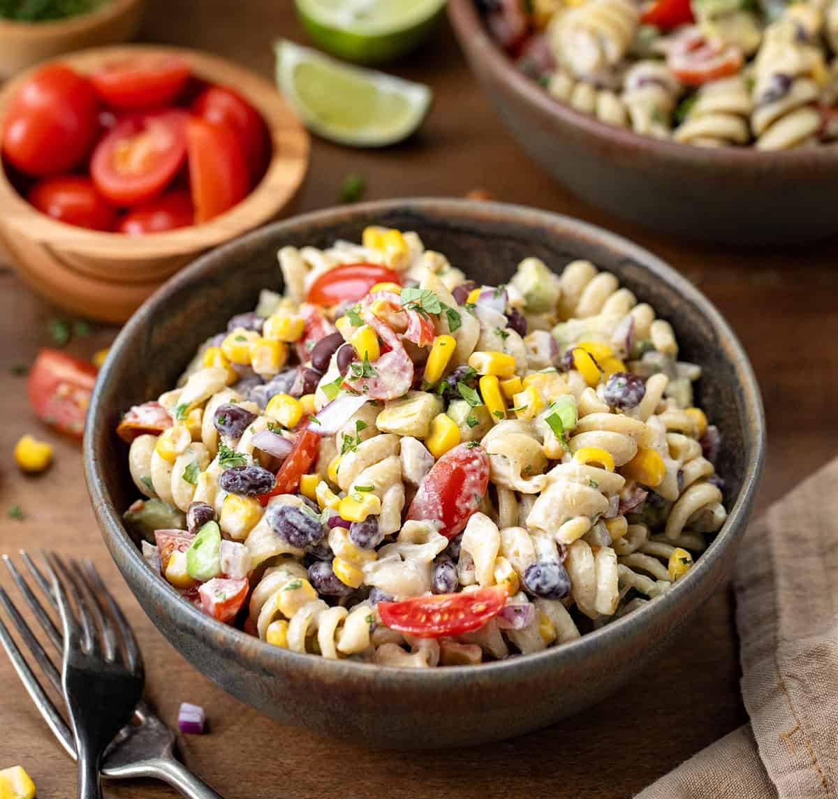 Bowls of Chipotle Lime Pasta Salad on a wooden table with fresh cut tomatoes close up.