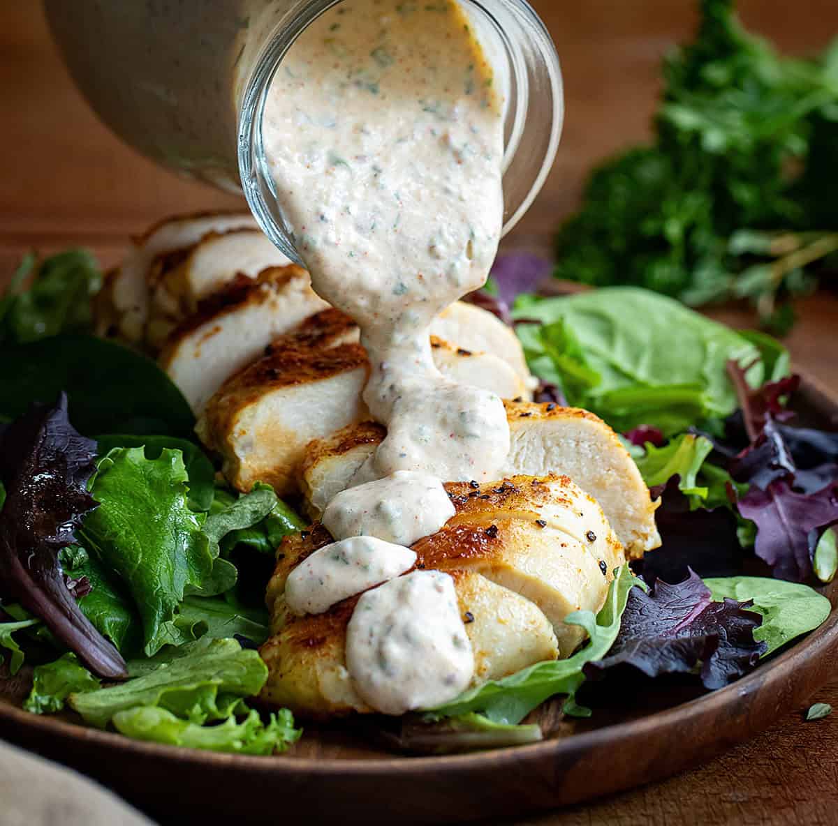 Pouring Cowboy Butter Ranch Dressing over sliced chicken breast on a salad.