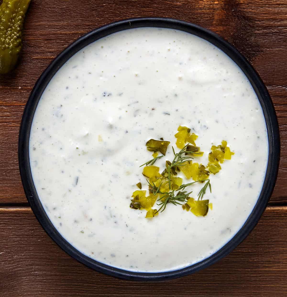 Bowl of Dill Pickle Ranch with finely diced pickled and fresh dill on a wooden table from overhead.