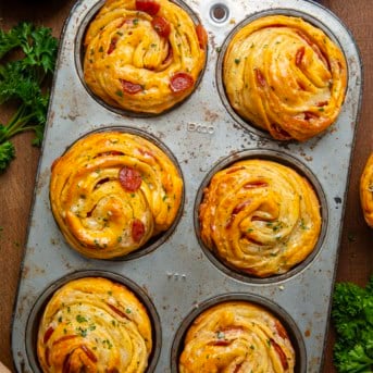 Pizza Cruffins in a muffin tin on a wooden table from overhead.