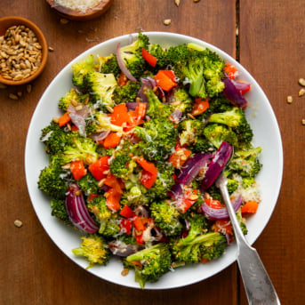 Roasted Broccoli Salad in a white bowl with a spoon on a wooden table from overhead.