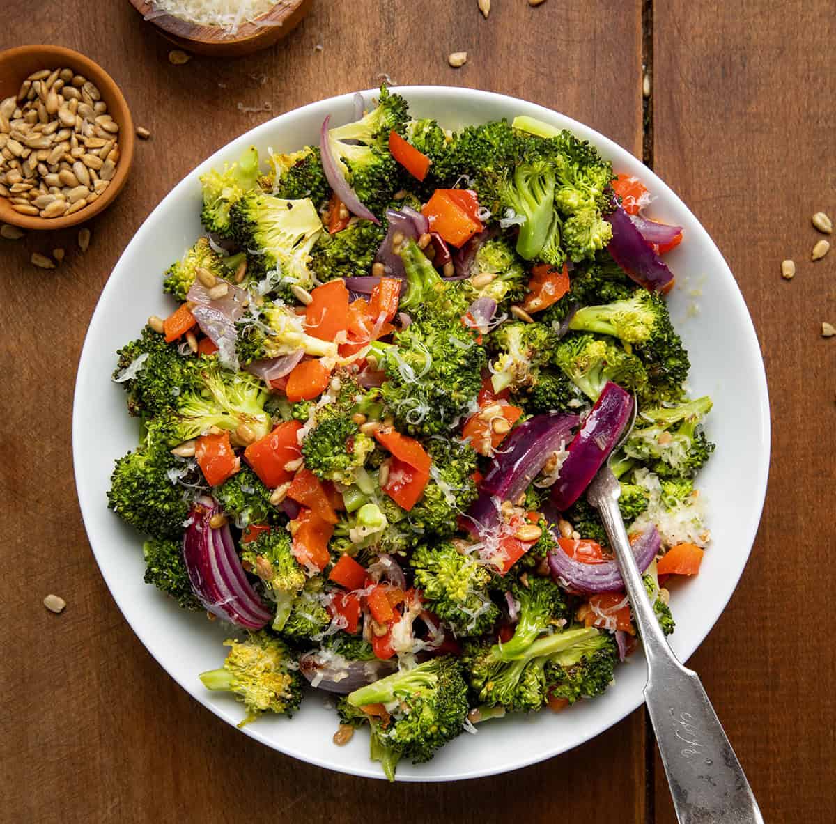 Roasted Broccoli Salad in a white bowl with a spoon on a wooden table from overhead.