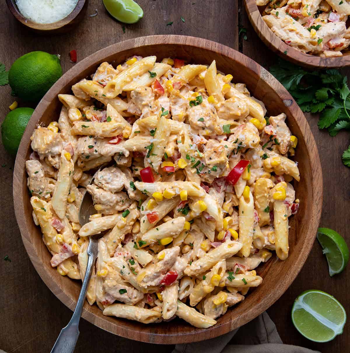 Bowls of Sriracha Chicken Pasta Salad with a spoon in them on a wooden table from overhead.