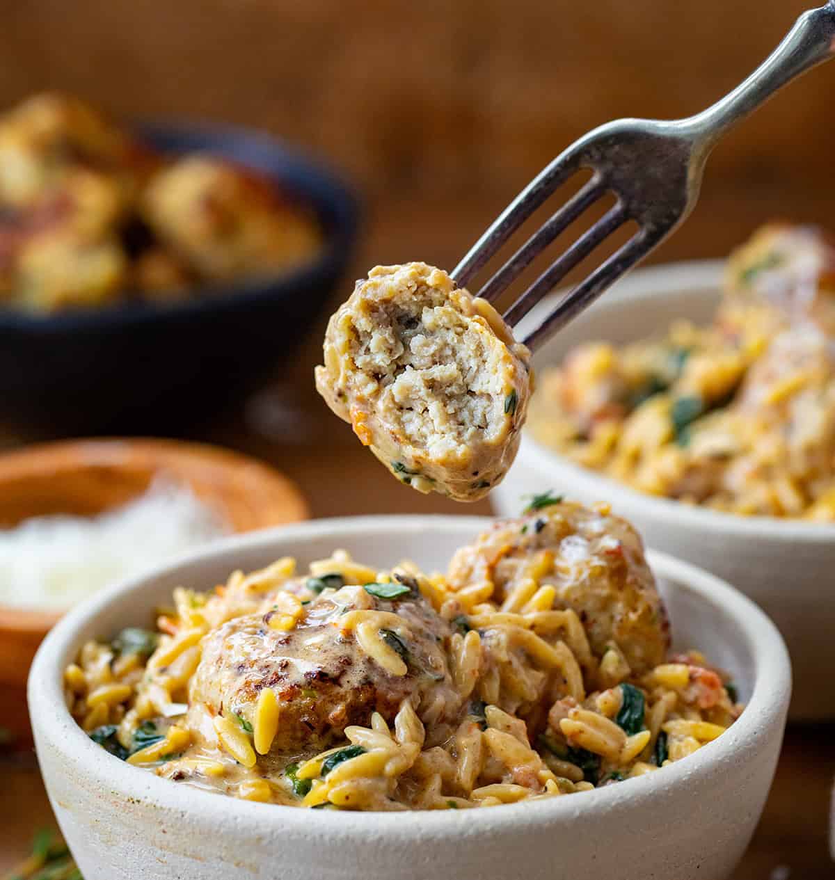 Fork holding a bit into Tuscan Chicken Meatball over a bowl of pasta.