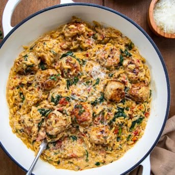 Skillet of Tuscan Chicken Meatball Orzo with a spoon in it on a wooden table from overhead.