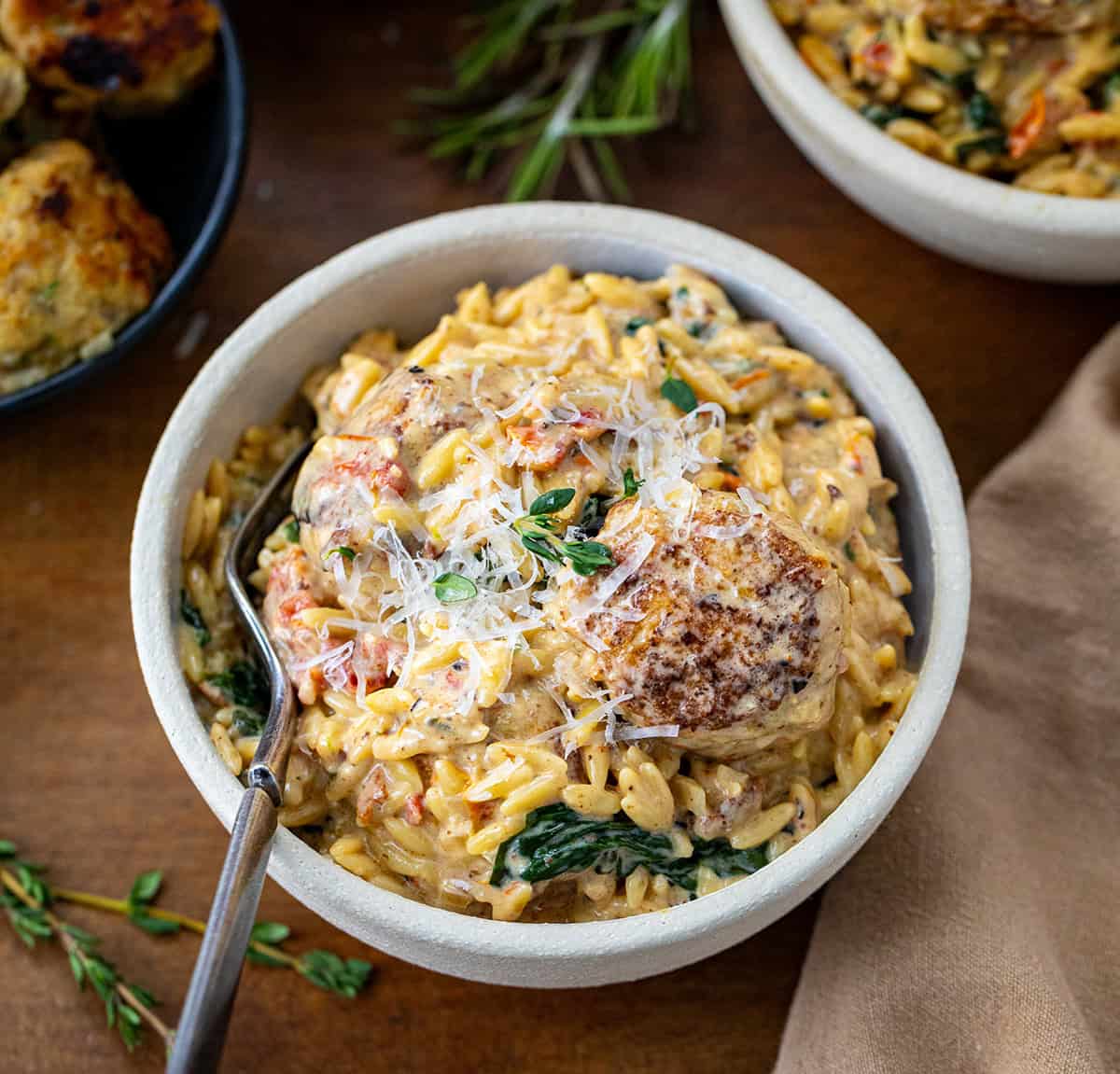 Bowl of Tuscan Chicken Meatball Orzo on a wooden table.