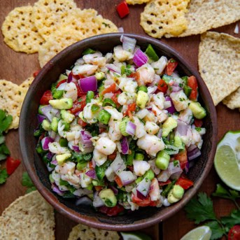 Bowl of Avocado Shrimp Ceviche surrounded by parmesan crisps on a wooden table from overhead.