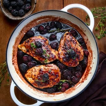 Skillet of Bourbon Blackberry Chicken on a wooden table from overhead with thyme and fresh blackberries.